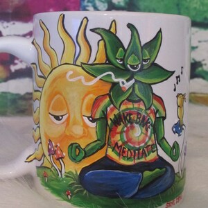 Puede incluir: Una taza de cerámica blanca con un diseño pintado a mano que presenta un sol con un ojo cerrado, una planta de marihuana verde con un ojo cerrado y las palabras "Wake Bake Meditate".
