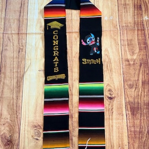 May include: Black graduation stole with colorful stripes and fringe. One side features the text "CONGRATS" with a graduation cap and scroll. The other side has an embroidered Stitch character with the text "Stitch".