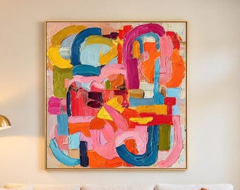May include: A large square canvas painting featuring thick, textured impasto brushstrokes in vibrant shades of pink, orange, yellow, blue, and green. The artwork is displayed in a thin wooden frame and hangs centered above a white sofa.