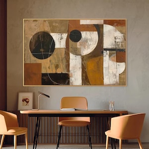 May include: Abstract art piece in a gold frame, featuring geometric shapes in brown, white, and black. The artwork hangs above a wooden desk with three orange chairs. A modern office setting.