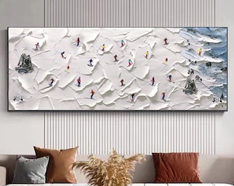 May include: A white abstract painting with a textured surface depicting a snowy mountain scene with skiers in colorful clothing. The painting is framed in a black frame and is hanging on a white wall.