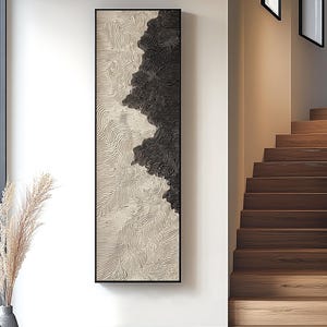 Può includere: Opera d'arte astratta da parete in una cornice nera. L'opera presenta un design strutturato con un contrasto di nero e bianco sporco, creando una divisione visiva. Il design è composto da linee curve e intricate.