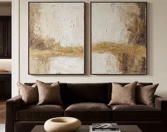May include: Two rectangular wall art pieces featuring thick, textured impasto paint in shades of white, cream, beige, and metallic gold. The abstract compositions display horizontal layers of color with heavy brushstrokes and raised paint surfaces.