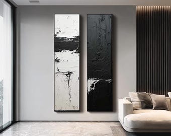 May include: Two vertical abstract paintings in black and white hang on a gray wall. The paintings have a textured, layered appearance, with thick brushstrokes creating a sense of depth. The artwork is framed in black.