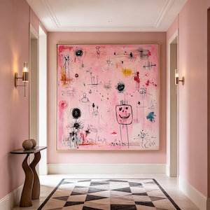 May include: A large square canvas painting featuring a light pink background with various black ink-style abstract doodles, including a prominent square-shaped face with a smile, displayed in a thin gold frame on a pink wall in a hallway.