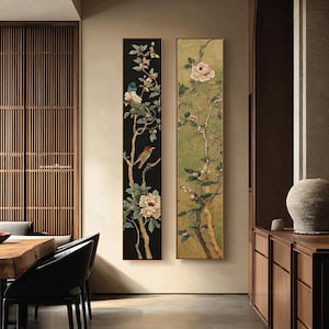 May include: Two vertical framed artworks. One has a black background with a floral and bird design. The other has a green background with a floral design. Both have a gold frame and are displayed on a neutral wall.
