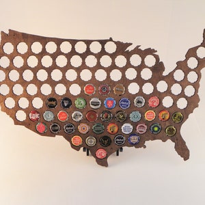 May include: A wooden map of the United States with a cutout for each state. The map is decorated with bottle caps from different breweries.