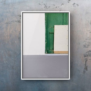 May include: A framed photograph of a white wall with a green door and a white panel. The wall is painted a light gray at the bottom.