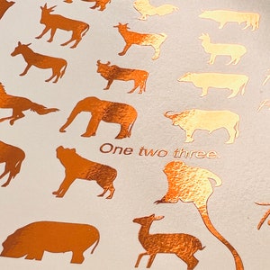 May include: A copper foil print featuring a variety of animal silhouettes, including a camel, giraffe, elephant, horse, and monkey. The print also includes the text "One two three" and "Testing."