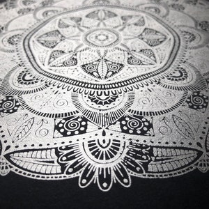 May include: Detailed silver mandala design on a black background. The intricate pattern features floral and geometric elements, creating a symmetrical and ornate artwork. The design is rendered in a metallic silver colour, providing contrast against the dark backdrop.