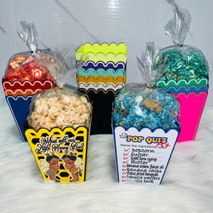 May include: Assortment of gourmet popcorn in colorful, decorative boxes. Flavors include red, blue, and green popcorn. One box features the text "What will our Little Honey Bee?" and another has a "Pop Quiz" with ingredients.