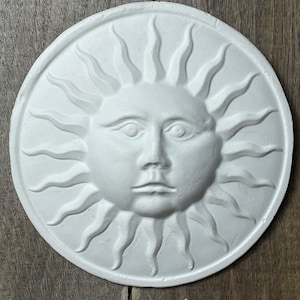 Puede incluir: Decoración de pared de sol de yeso blanco con una cara y rayos.