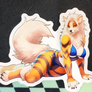 May include: A sticker featuring a furry, orange and white animal wearing a blue and white swimsuit. The animal has a long, bushy tail and is lying on its side with its head turned to the side.