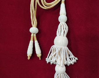 Peut inclure: Un pompon blanc perlé avec un cordon doré. Le pompon a deux couches de perles et une longue frange fluide.