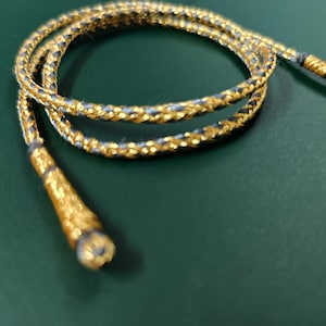Puede incluir: Un cordón trenzado dorado y azul con dos extremos de borla.