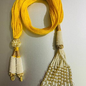 May include: A yellow cord with two white and gold tassels. The tassels are made of small beads and have a gold accent at the top.