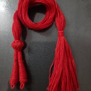 Könnte beinhalten: Eine rote Quaste mit zwei Quasten an einem Ende und einer einzelnen Quaste am anderen Ende.