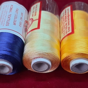 May include: Four spools of thread in yellow, blue, beige, and teal. The spools are labelled "Komal Textiles" and "Fast Colour".