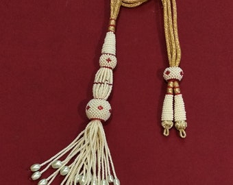 Peut inclure: Un collier de perles blanches avec un pompon et des accents rouges. Le collier a un cordon doré et est sur un fond rouge.