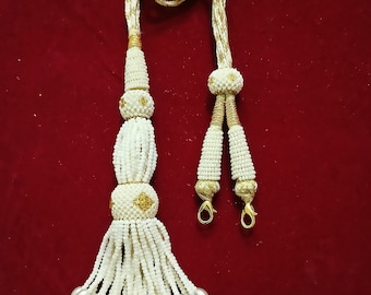 Peut inclure: Un collier de perles blanches avec des accents dorés. Le collier a un long cordon et deux glands avec des perles décoratives.
