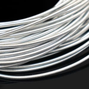 May include: A close-up of a silver-colored, flexible wire with a beaded texture. The wire is coiled and arranged in a spiral pattern.