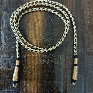 May include: A black and gold braided cord with tassels on each end.