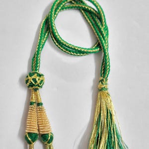 Könnte beinhalten: Dekorative Kordel in Grün und Gold mit Quasten. Die Kordel besteht aus gedrehten grünen und goldenen Fäden. Die Quasten sind goldfarben mit grünen Akzenten. Ideal für Dekorationen und Bastelarbeiten.