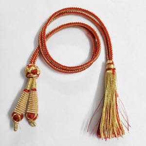 May include: A decorative red and gold cord with a tassel and two smaller tassels. The cord is braided with a gold thread and has a gold tassel at the end. The smaller tassels are gold with red accents.