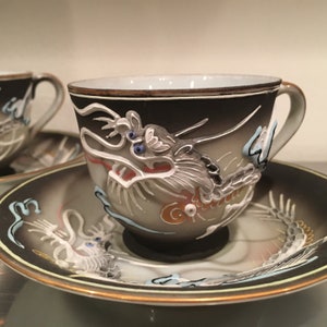 Op de afbeelding: Een set van twee vintage theekopjes en schoteltjes met een zwart-wit drakenontwerp. De kopjes en schoteltjes zijn gemaakt van porselein en hebben een gouden rand.