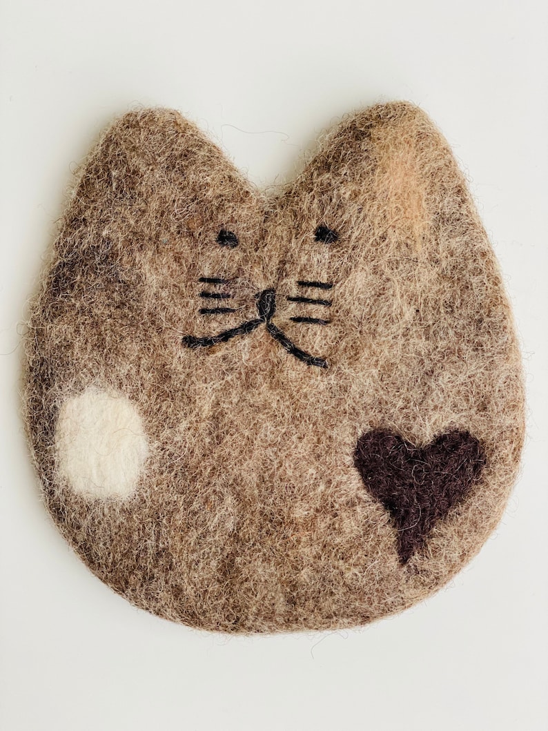 May include: A brown felt cat with a white spot and a brown heart. The cat has black embroidered eyes and whiskers.