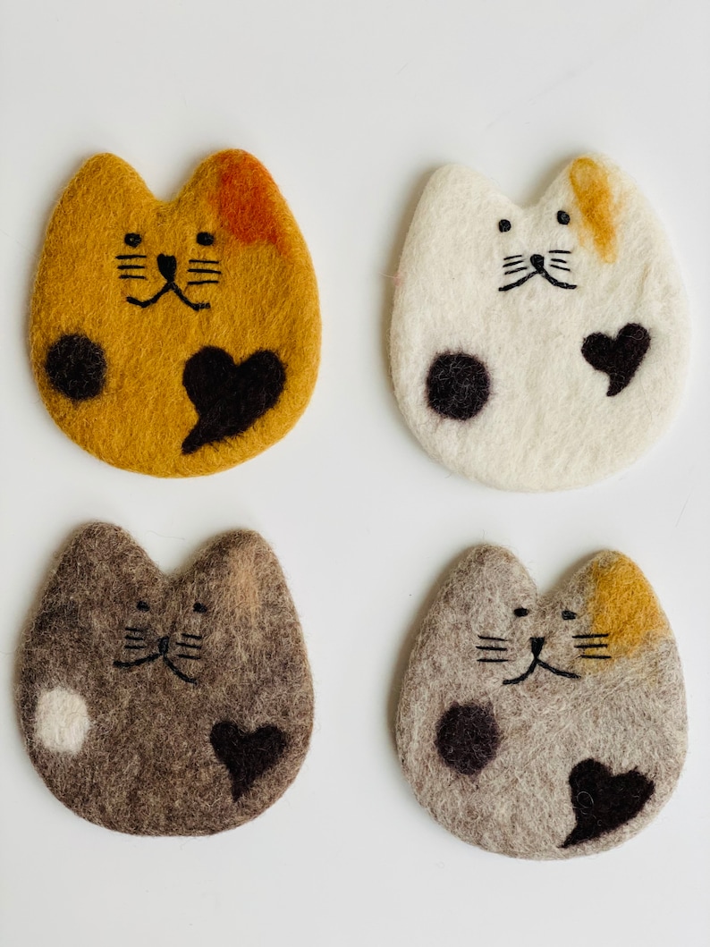 May include: Four felt cat coasters in different colors and patterns. Each coaster features a black embroidered heart and black embroidered cat face.