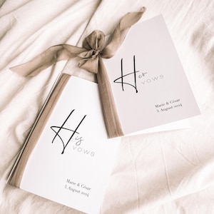 以下が含まれることがあります： 「His Vows」と「Her Vows」の文字が黒いエレガントな筆記体で書かれた2冊の結婚誓約書。 「Marie & César」と日付「2024年8月3日」も印刷されています。 茶色のリボンが小冊子をまとめ、白い背景に配置されています。
