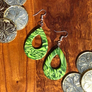 May include: A pair of green and white dangle earrings with a teardrop shape and a hole in the centre. The earrings are made of polymer clay and have a marbled effect.