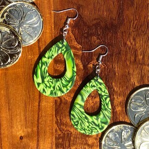 May include: A pair of green and yellow dangle earrings with a swirl pattern. The earrings are made of polymer clay and have a silver hook.