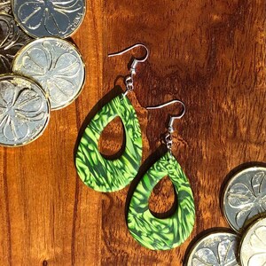 May include: A pair of green and black teardrop-shaped earrings with a swirl pattern. The earrings have silver hooks.