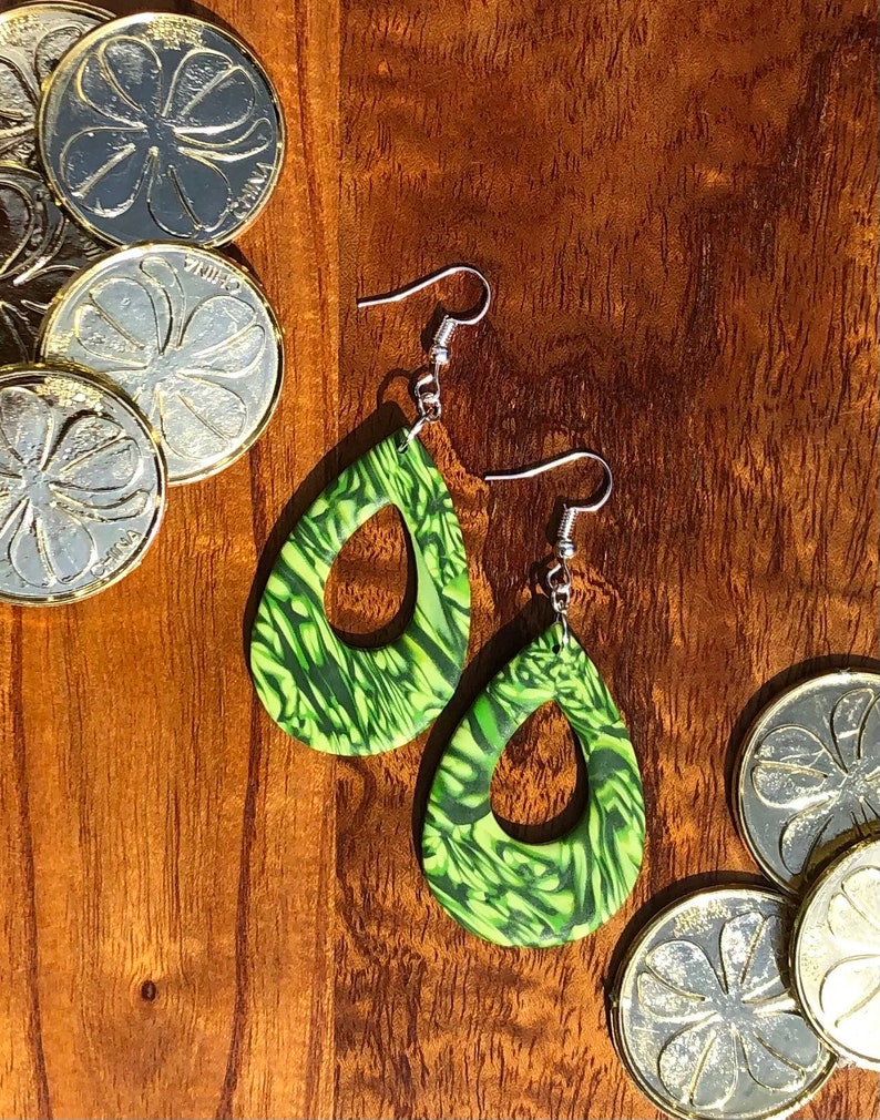 May include: A pair of green and black teardrop-shaped earrings with a swirl pattern. The earrings have silver hooks.