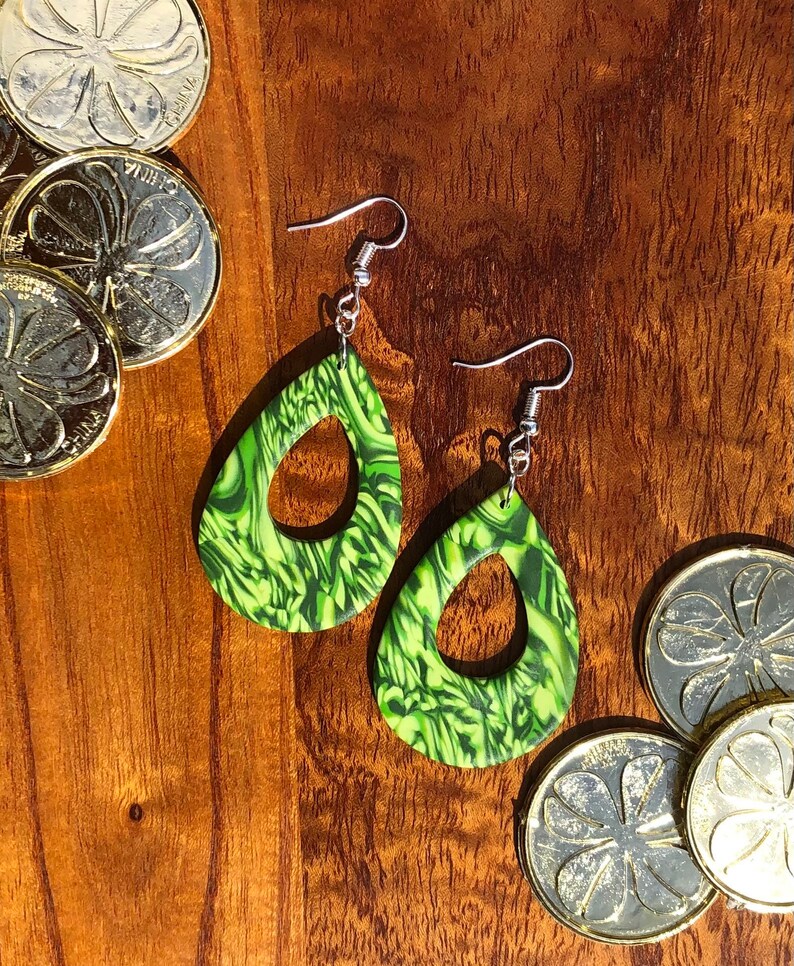 May include: A pair of green and black marbled teardrop-shaped earrings with silver hooks. The earrings have a swirl pattern and a hole in the centre.