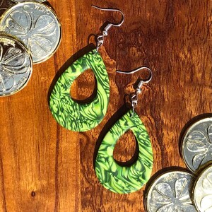 May include: A pair of green and white teardrop-shaped earrings with a swirl pattern. The earrings have silver hooks.