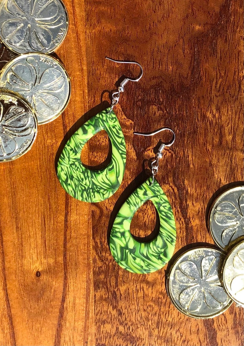 May include: A pair of green and white teardrop-shaped earrings with a swirl pattern. The earrings have silver hooks.