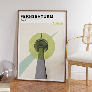 May include: A framed poster with a minimalist design featuring a green and grey illustration of the Fernsehturm, a television tower in Berlin, Germany. The poster includes the text "Fernsehturm" and "Berlin" in black text and "1969" in white text.