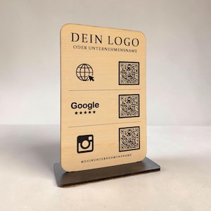 Może przedstawiać: Drewniany szyld biznesowy z napisem "DEIN LOGO ODER UNTERNEHMENSNAME" na górze. Zawiera ikony strony internetowej, Google i Instagram, każda w parze z kodem QR. Szyld stoi na ciemnobrązowej podstawie.