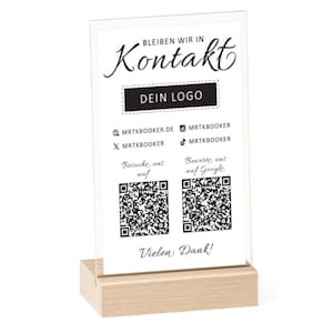 Könnte beinhalten: Ein weißes Acrylschild mit schwarzem Text, der "Bleiben wir in Kontakt" und "Dein Logo" lautet. Das Schild enthält auch Social-Media-Icons und QR-Codes, um eine Website zu besuchen und eine Bewertung auf Google abzugeben. Das Schild steht auf einem Holzsockel.