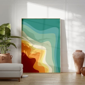 Op de afbeelding: Abstracte kunstprint met een gelaagd ontwerp in oranje, geel, groen en blauwe kleuren. De print is ingelijst in een dun gouden lijst en hangt aan een witte muur.