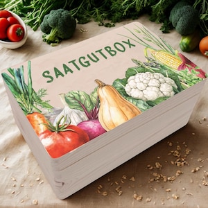 Könnte beinhalten: Eine Holzkiste mit hellbrauner Oberfläche und einer bunten Illustration verschiedener Gemüse und Kräuter. Die Kiste ist mit "SAATGUTBOX" in grüner Schrift beschriftet.