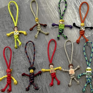 May include: Ten colorful keychains featuring miniature Lego figures attached to paracord loops. The figures include a superhero, a construction worker, a police officer, and others.