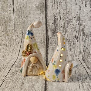 Pu&ograve; includere: Due statuette di gnomi in ceramica con cappelli color crema decorati con macchie di vernice colorate. Uno ha la barba e un accento di foglie di agrifoglio. L'altro ha dei fori nel cappello che emettono un bagliore caldo.