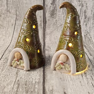 Pu&ograve; includere: Due statuette di gnomi in ceramica con cappelli conici smaltati verdi e marroni. I cappelli hanno volute decorative e ritagli a forma di stella che si illuminano. Ogni gnomo ha una base bianca ad arco con una piccola figura e foglie di agrifoglio.