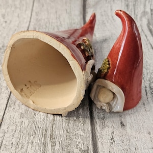 Pu&ograve; includere: Due statuette di gnomi in ceramica con cappelli rossi e barbe bianche. Uno gnomo &egrave; in posizione verticale, l'altro &egrave; capovolto. L'interno del cappello dello gnomo &egrave; beige. Gli gnomi hanno un aspetto rustico e fatto a mano.