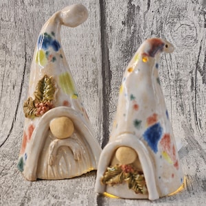 Pu&ograve; includere: Due statuette di gnomi in ceramica con cappelli alti e curvi. I cappelli sono macchiati di vernice blu, gialla e rossa. Ogni gnomo ha un viso rotondo e una caratteristica simile alla barba. Uno gnomo ha un accento decorativo di foglie e bacche.