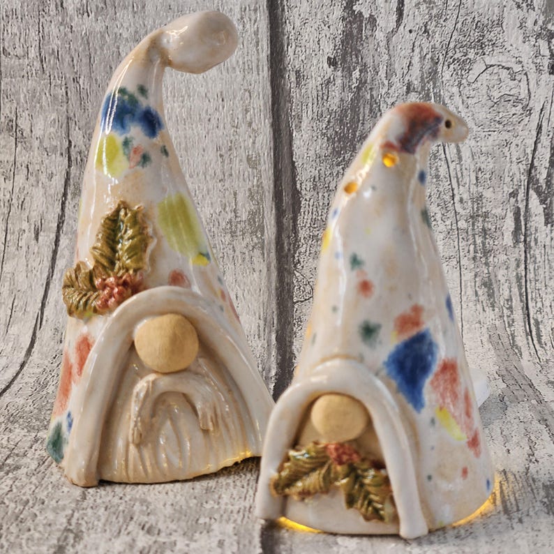Pu&ograve; includere: Due statuette di gnomi in ceramica con cappelli alti e curvi. I cappelli sono macchiati di vernice blu, gialla e rossa. Ogni gnomo ha un viso rotondo e una caratteristica simile alla barba. Uno gnomo ha un accento decorativo di foglie e bacche.